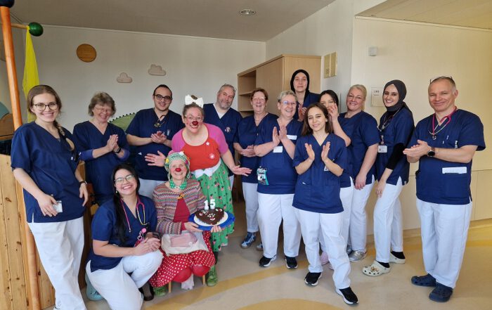 Das Team der Kinderklinik mit den Clowns. Antonella hat einen Kuchen mit der Zahl 15 dabei.