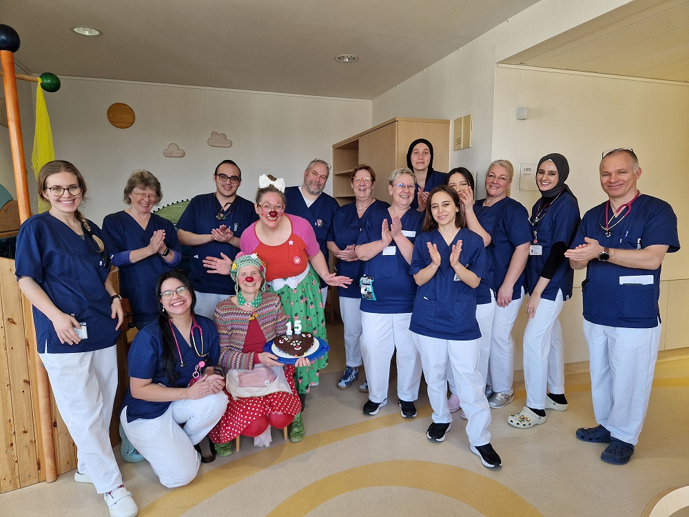 Das Team der Kinderklinik mit den Clowns. Antonella hat einen Kuchen mit der Zahl 15 dabei.