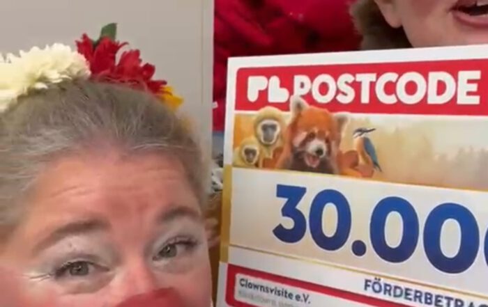 Clowns halten einen Scheck vors Gesicht, die Zahlen 30.000 steht drauf von der Postcode Lotterie