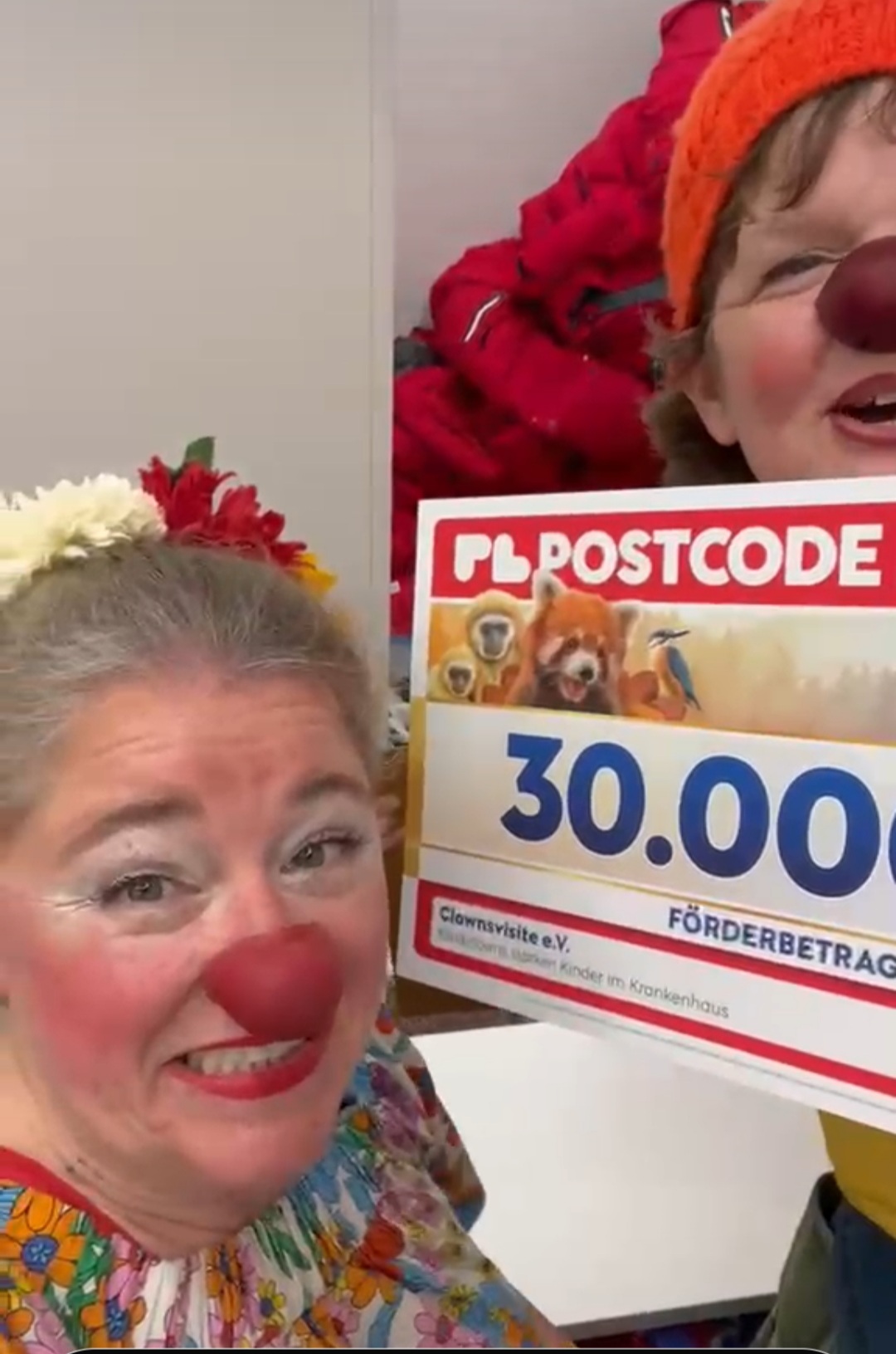 Clowns halten einen Scheck vors Gesicht, die Zahlen 30.000 steht drauf von der Postcode Lotterie